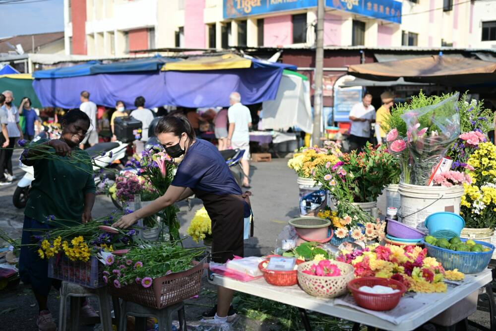 A woman arranges flowers in a bustling outdoor market.